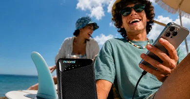 Two travelers on a beach staying online and charging a phone with one pocket Noomi device